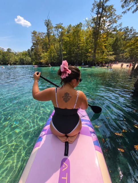 Paddle surf en agua turquesa con coleta rosada en el pelo